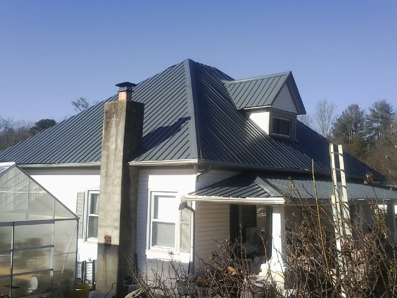 Dark blue standing seam metal roof on a white farmhouse with dormer — Slate & Tile Roof Repair by Roofing Brothers in Deforest