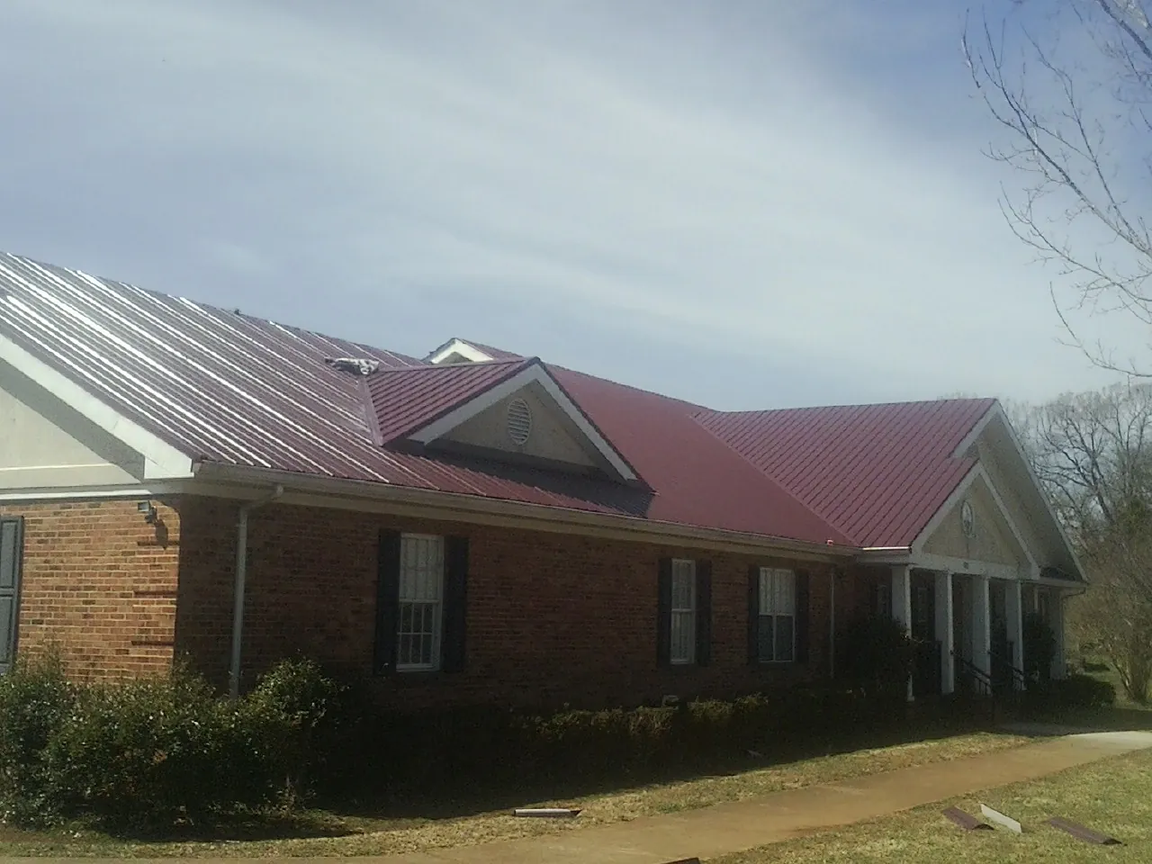 Red metal roof with gabled entries on a long brick building, from a Hail Damage Roof Repair job in Deforest