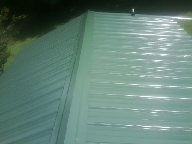 New green metal panels meeting at the ridge of a roof — Flat Roof Repair work by our crew in Deforest