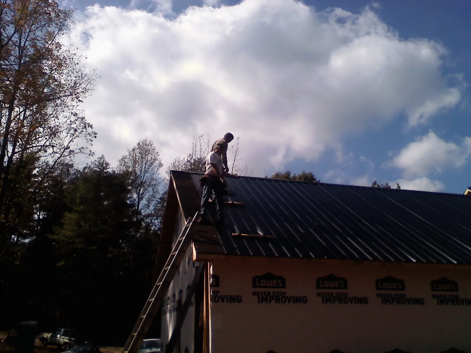Roofer fastening dark metal panels high against a cloudy sky, from a Roof Inspection job in Deforest