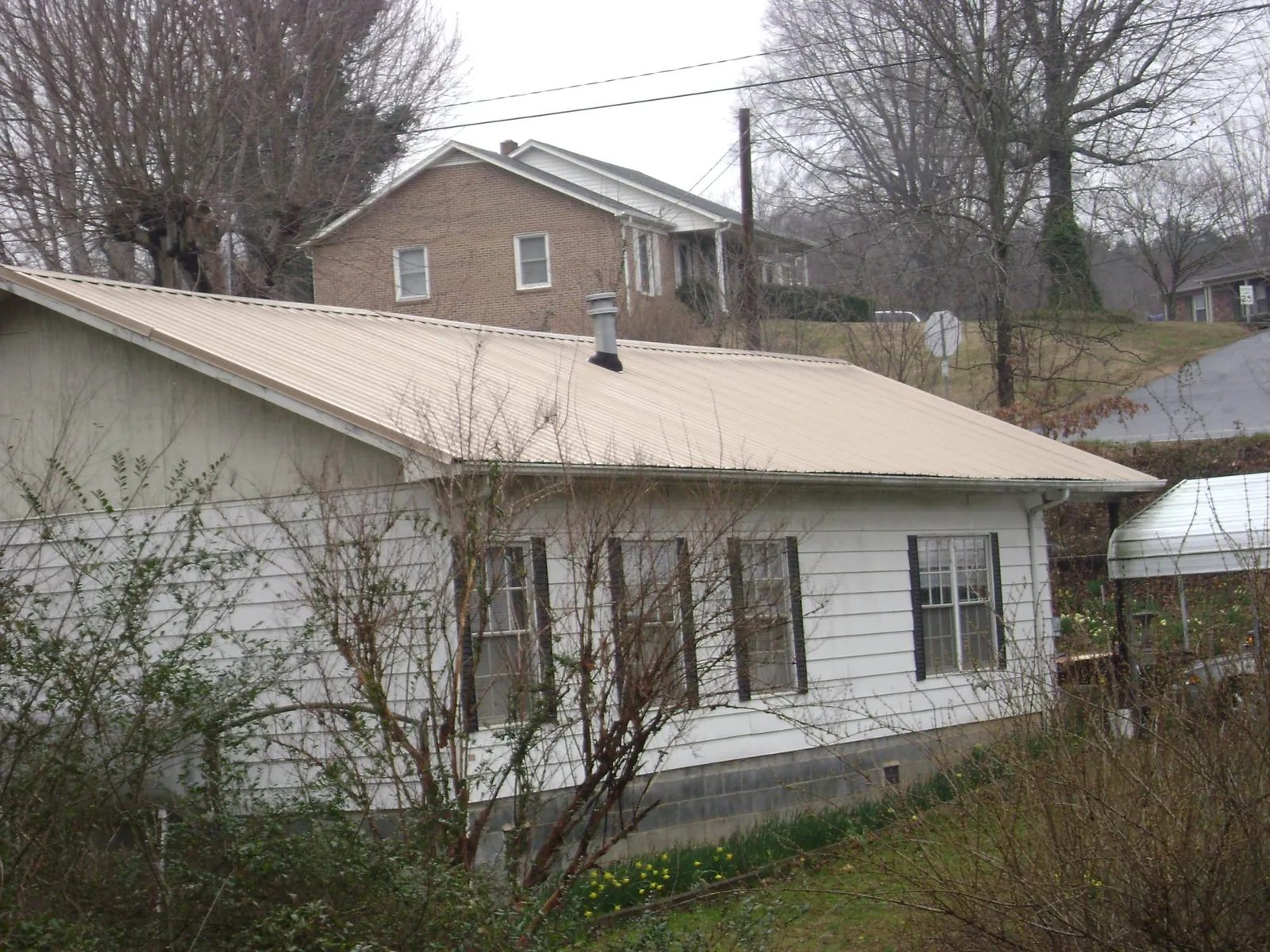 Tan metal roof on a white sided house set into a hillside — Commercial Roofing by Roofing Brothers in Deforest